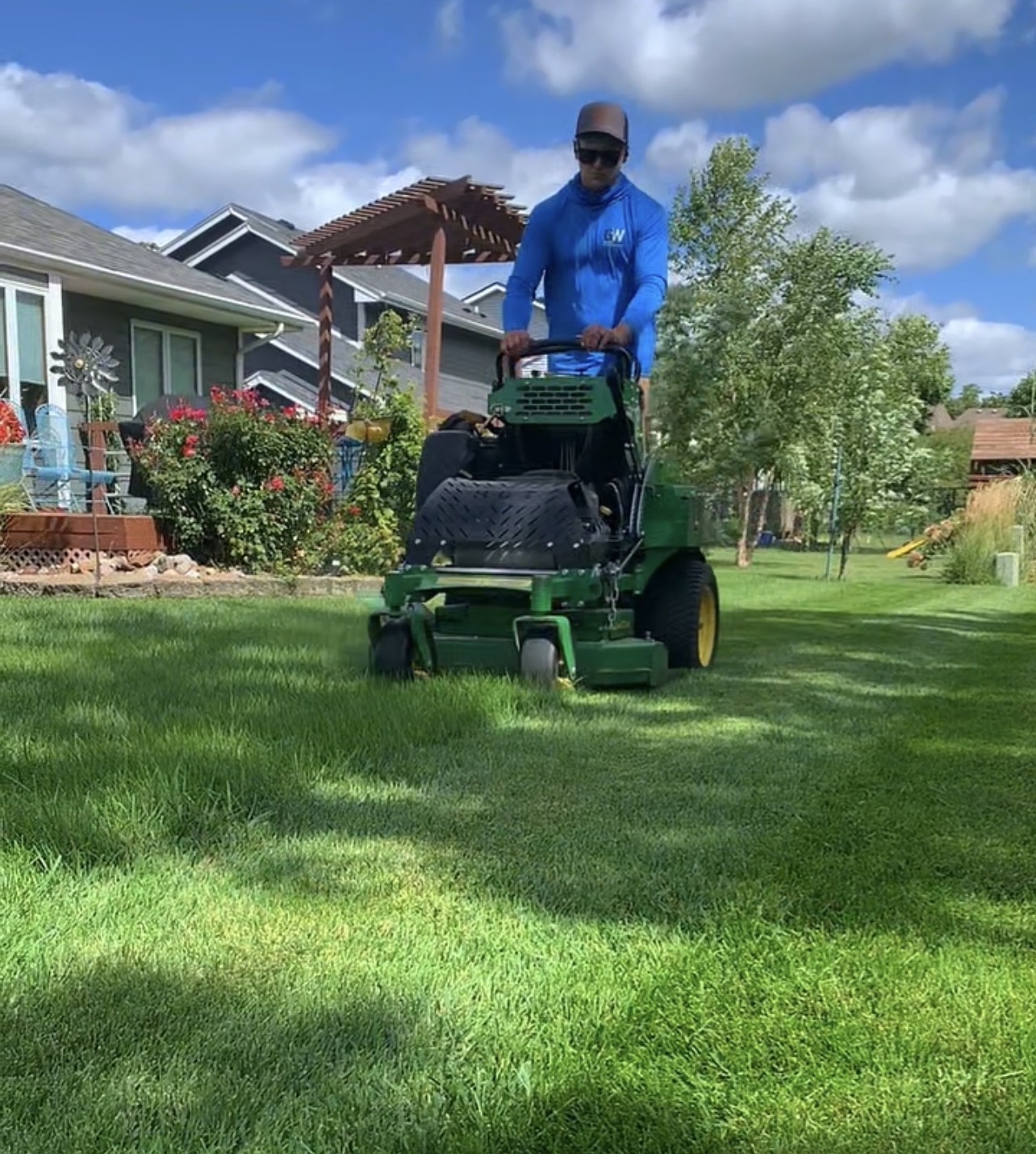 Operator on a green John Deere zero turn mower in an Ankeny backyard